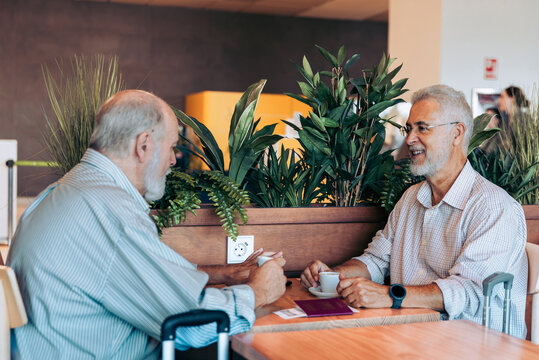Elderly friends with coffee chatting at airport cafe - Powered by Adobe