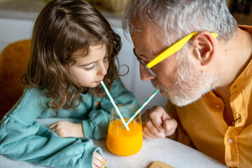Senior man and girl drinking fruit juice on table