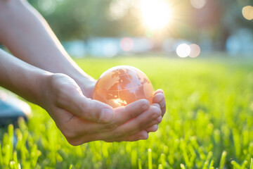 Concept of environment world Earth Day: glass globe in kid hands on blurred green grass banner...
