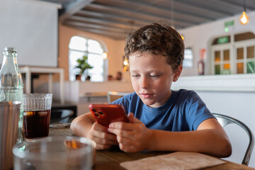 Boy playing on smart phone in restaurant