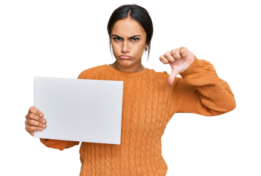 Young brunette woman holding blank empty banner with angry face, negative sign showing dislike with thumbs down, rejection concept