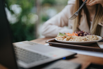 Cropped photo of businesswoman having breakfast early in the morning while working on her lap top in city office.