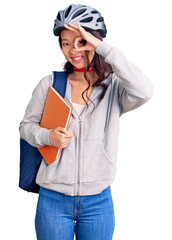 Young beautiful chinese girl wearing student backpack and bike helmet holding book smiling happy doing ok sign with hand on eye looking through fingers