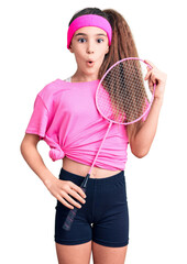Cute hispanic child girl holding badminton racket scared and amazed with open mouth for surprise, disbelief face