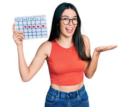 Young hispanic woman holding heart calendar celebrating achievement with happy smile and winner expression with raised hand - Powered by Adobe