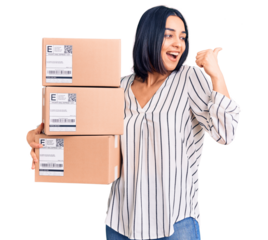 Young beautiful latin woman holding delivery package pointing thumb up to the side smiling happy with open mouth