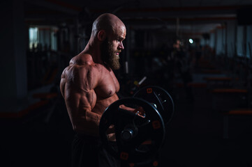 Fototapeta na wymiar Caucasian bald topless man doing an exercise with a barbell in the gym. Bicep curls with weights.