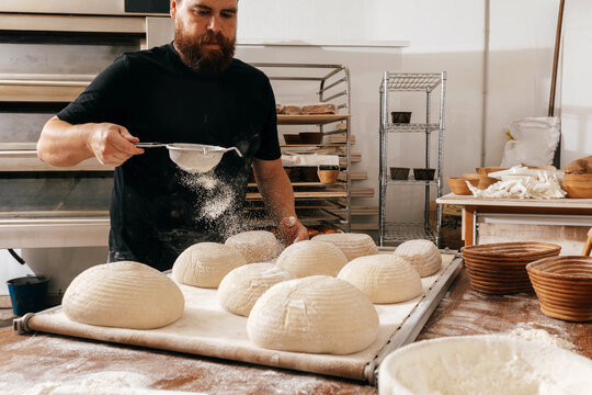 Focused man sifting flour on dough in kitchen