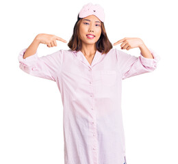 Young beautiful chinese girl wearing sleep mask and pajama looking confident with smile on face, pointing oneself with fingers proud and happy.