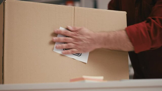 Warehouse worker putting fragile item sticker on box, packing orders in office
