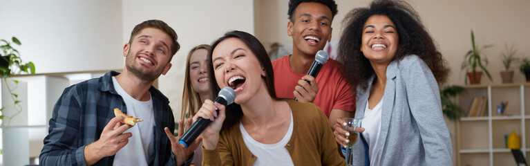Young asian girl holding microphone and singing while playing karaoke with best friends at home....