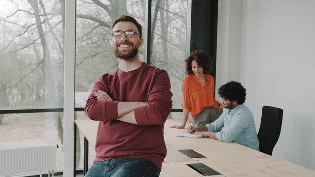 Confident portrait of Caucasian handsome stylish man in casual wear, wearing trendy glasses, smiling looking confidently at camera standing in corporate office. People. Corporate business. Profession