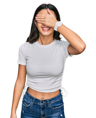 Young hispanic girl wearing casual white t shirt smiling and laughing with hand on face covering eyes for surprise. blind concept.