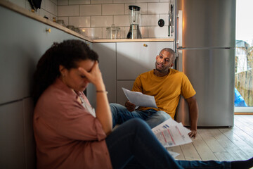 Stressed upset couple going over bills on kitchen floor