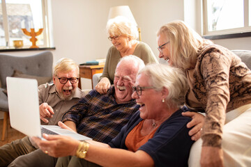 Diverse senior people sitting at home laughing with laptop