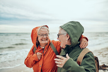 Two happy old female friends walking on the cold beach