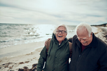 Happy senior man and woman old elderly couple walking on cold beach
