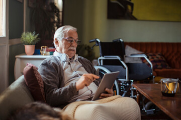 Disabled senior man sitting on couch using smartphone at home
