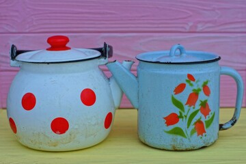 two dirty,kitchen different blue and white with drawings of old rusty closed empty classic for boiling water with a lid of a home enameled kettle stand on a yellow wooden table 