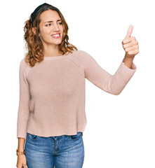 Beautiful young caucasian woman wearing casual sweater looking proud, smiling doing thumbs up gesture to the side