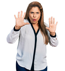 Middle age latin woman wearing business shirt afraid and terrified with fear expression stop gesture with hands, shouting in shock. panic concept.