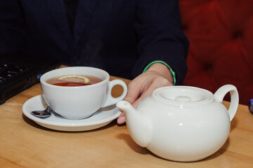 Female hands holding white porcelain tea set with hot tea with lemon standing on table in café 