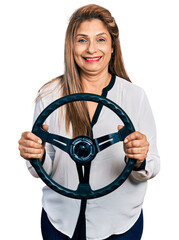 Middle age latin woman holding steering wheel smiling with a happy and cool smile on face. showing...