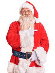 Old senior man with grey hair and long beard wearing traditional santa claus costume cheerful with a smile on face pointing with hand and finger up to the side with happy and natural expression