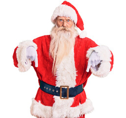 Old senior man with grey hair and long beard wearing traditional santa claus costume pointing down with fingers showing advertisement, surprised face and open mouth