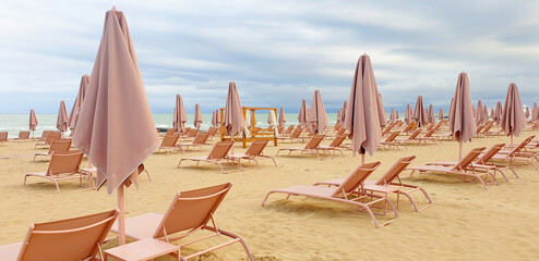 Empty beach with beige umbrellas and sun loungers before rain in summer. Panorama.