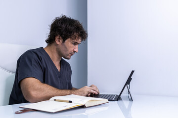 A male nurse is in the office looking at his laptop while calendaring his next clients.
