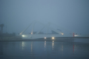 Valencia, Spain - November 18, 2023: Swing bridge in Marina Valencia. People walk along the bridge during heavy fog.