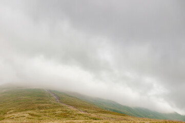 Photo of the summit of a mountain immersed in a cloud, with a damp autumn landscape.