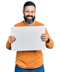 Hispanic man with beard holding blank empty banner smiling and laughing hard out loud because funny crazy joke.