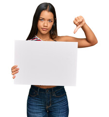 Beautiful hispanic woman holding blank empty banner with angry face, negative sign showing dislike...
