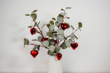 closeup eucalyptus branches decorated with red heart ornaments for christmas ,greeting festive card