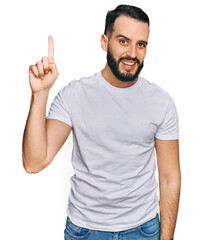 Young man with beard wearing casual white t shirt pointing finger up with successful idea. exited and happy. number one.