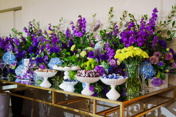 Table with sweets and cakes decorated with bouquets of purple flowers. 