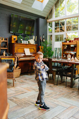 Fototapeta premium Funny little boy in plaid shirt and jeans in the interior of a country house. 