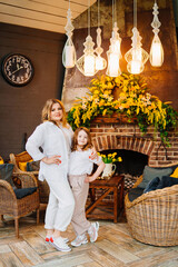 Mother and daughter in a room by the fireplace in comfortable light clothes. 