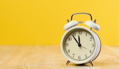 Round white alarm clock, the time is five minutes to twelve. Yellow background