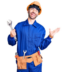 Young hispanic man wearing electrician uniform holding wrench celebrating victory with happy smile and winner expression with raised hands