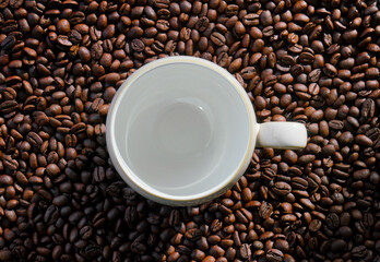 Empty coffee mug on coffee beans background with dramatic light and copy space
