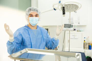 Guy staff of veterinary clinic begins working day - young man doctor in entire perfect surgical suit stands with raised hands in gloves