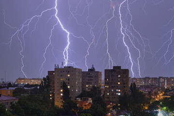 Multiple lightning strikes and thunderstorm over city buildings, at night. Weather phenomena.