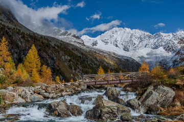 Fototapeta na wymiar The alpine creek flow in front of the highness of the snow capped Alps.