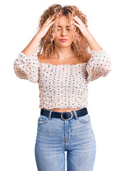 Young blonde woman with curly hair wearing casual clothes suffering from headache desperate and stressed because pain and migraine. hands on head.