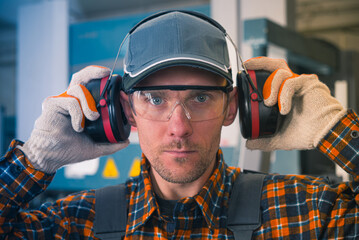 Hearing protection. A factory worker puts on noise-cancelling earmuffs. Work safety theme.