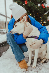 A beautiful young girl hugging her white dog in winter, Festive New Year's mood, happy woman with a dog at Christmas time