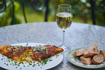 Delicious french style omelette with cheese, sprinkled by fresh chives, served outside in the garden with glass of white wine and pieces of whole grain baguette as a light lunch in sunny summer day.